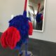 Red and blue feathered stuffed ostrich looking at its reflection in a long mirror