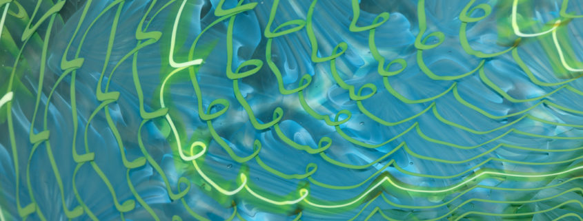 Blue and neon green squiggle designs on a detail of a blown glass bowl.