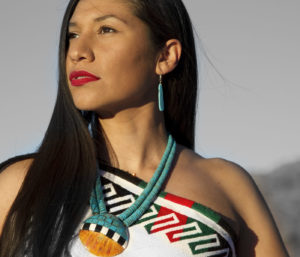 Female identified Indigenous person in a color portrait wearing a beaded necklace and sleeveless top
