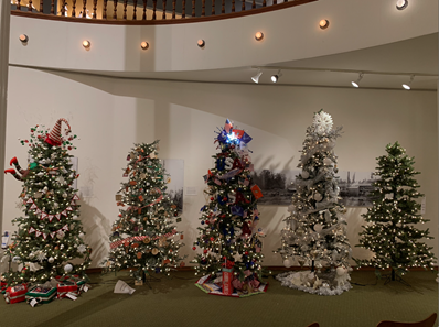 Five decorated Christmas trees lined up along a wall