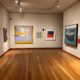 Museum gallery with abstract paintings hanging on the wall and a pedestal with a black abstract sculpture