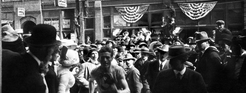 Black and white photo of a man running in a crowd of spectators in 1913.