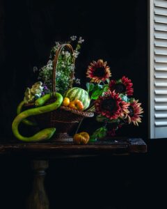 Color still photograph of red sunflowers., fruit and vegetables in a basket.